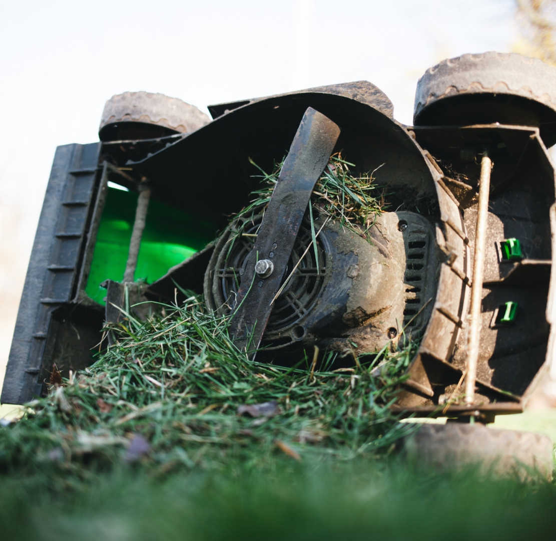 Underside of lawn mower covered with built-up grass clippings and blade visible